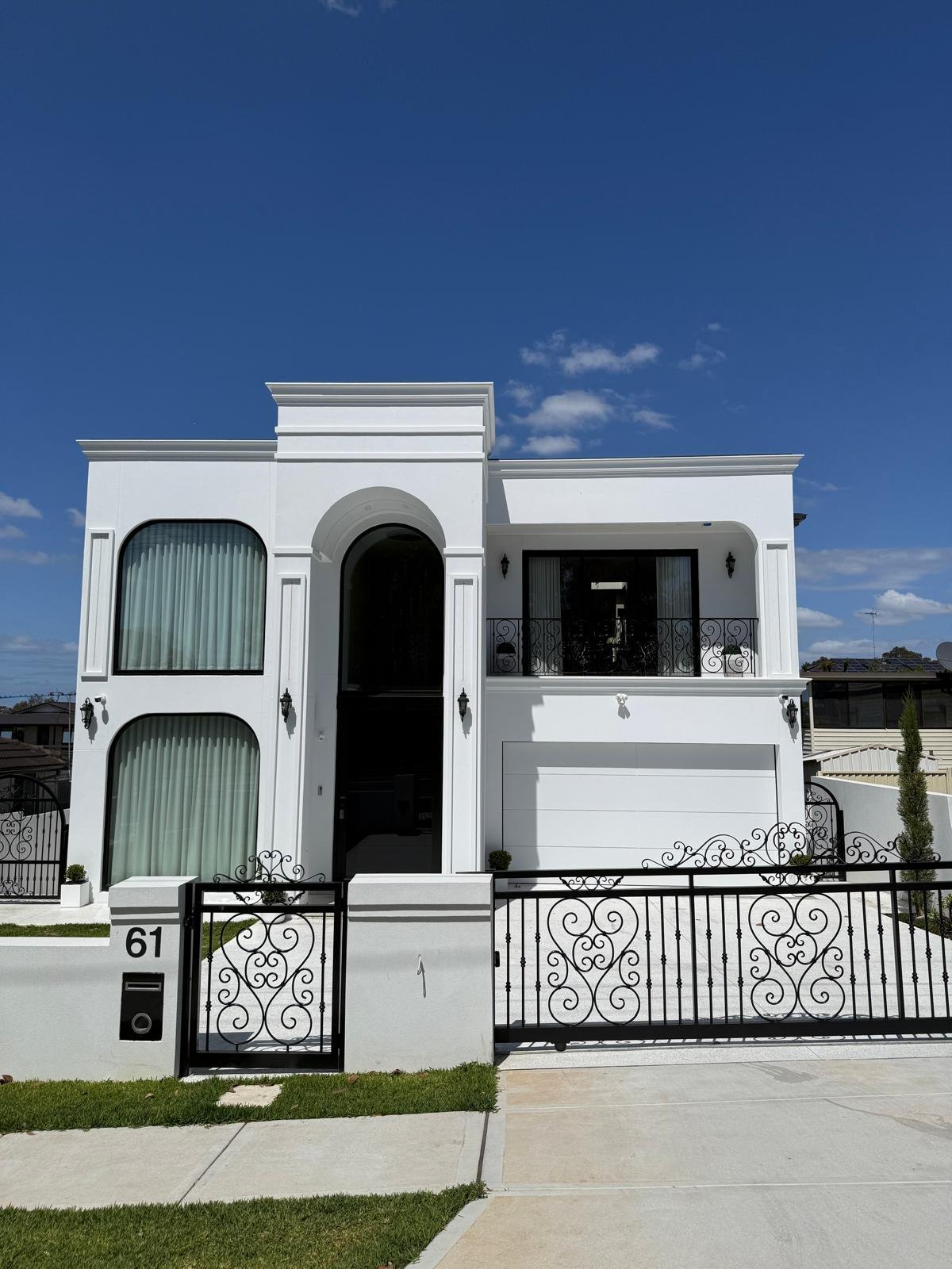 Front elevation of the white residence with arched glazing and detailed gates