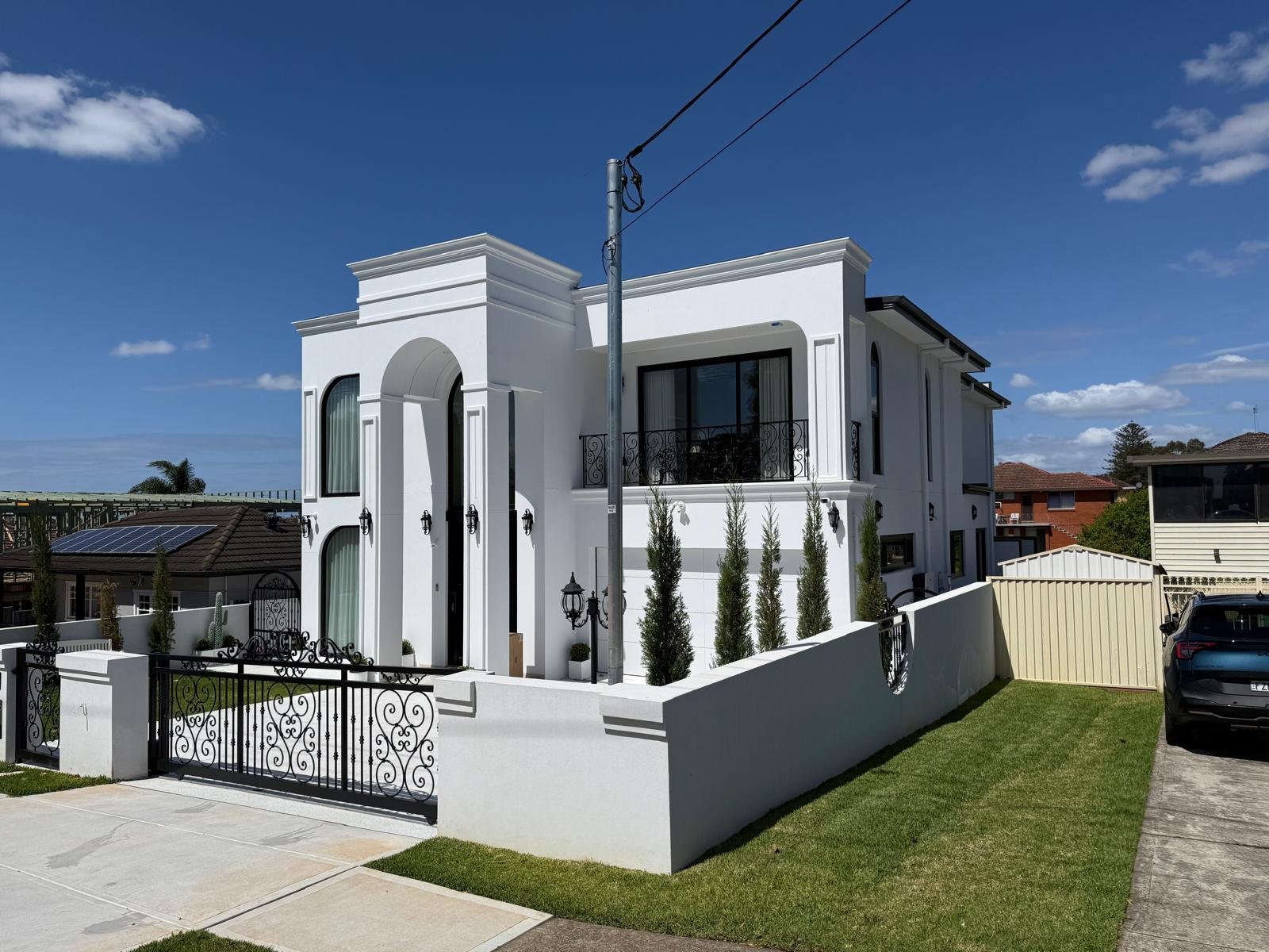White two-storey residence with an arched entrance, black ironwork and a landscaped side elevation